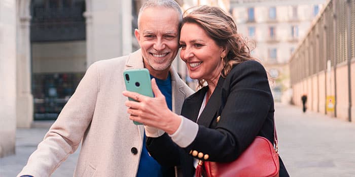 Ein lächelnder Mann und eine lächelnde Frau machen draußen in einer Stadt gemeinsam ein Selfie.