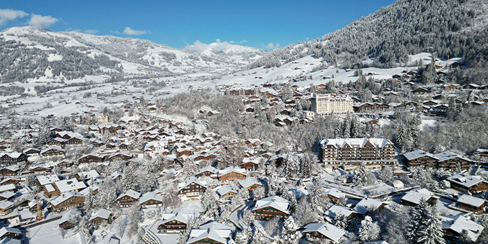 Aerial view of a snow-covered town nestled in a valley surrounded by mountains under a clear blue sky.